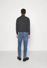 Mörkgrå långärmad tröja med hög krage, tillsammans med ljusblå slim-fit jeans och svarta skor, sedd bakifrån.