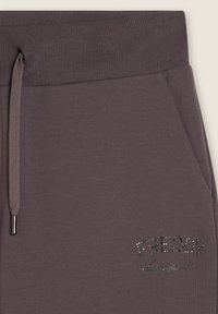 Pantalones deportivos grises con cinturilla acanalada, con cordón ajustable y un logo decorado con pedrería. Textura suave, diseño casual.