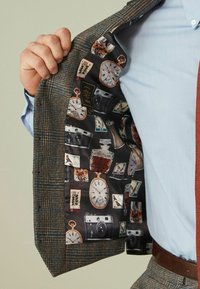 Brauner Karo-Blazer mit strukturiertem Äußeren. Das Innere besteht aus schwarzem Stoff mit Drucken von Vintage-Kameras, Uhren und Postkarten.