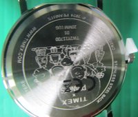 Dos de montre-bracelet Timex montrant des chefs de dessin animé gravés, numéro de modèle, dos en acier inoxydable et URL du site web sur un fond vert.
