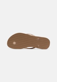 Sola de chinelo castanho com superfície texturizada e dois buracos circulares para as alças. Feito de borracha, apresentando uma forma plana e arredondada.