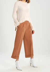 Beige ribbad tröja med långa ärmar, matchad med bruna vida byxor med veck och mudd, kompletterade med vita ankelboots.