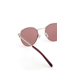 Okulary przeciwsłoneczne w okrągłym kształcie z jasnoróżowymi soczewkami, cienką złotą metalową oprawą i burgundowymi zausznikami z acetatu. Wyposażone w przezroczyste noski dla komfortu.