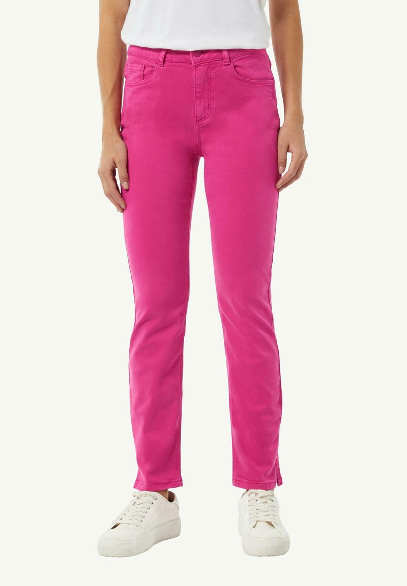 Dopasowane różowe spodnie bawełniane z pięcioma kieszeniami, szlufkami na pasek i prostym krojem, w połączeniu z białymi trampkami.