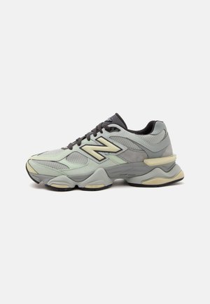 Сив и бежов маратонка New Balance с мрежести и велурени панели, дебела подплатена подметка и черни връзки на обикновен светъл фон.