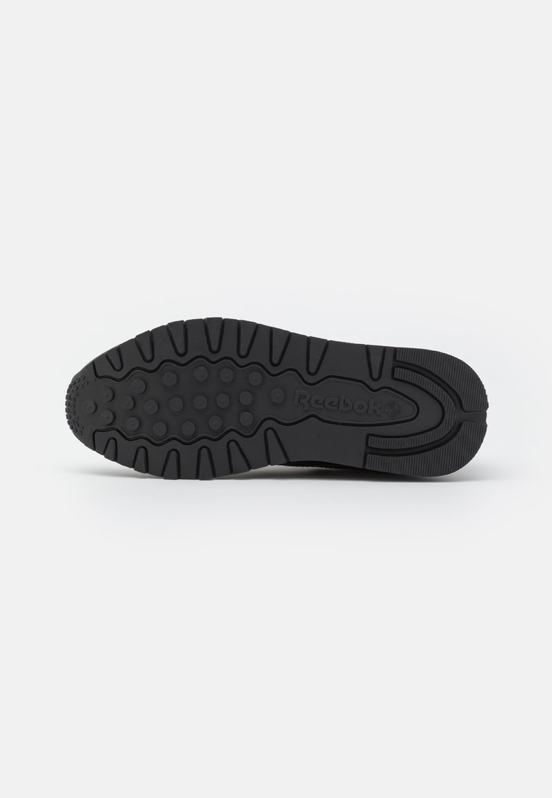 Black athletic shoe sole featuring patterned tread for traction, textured rubber material, and logo detailing on the side.