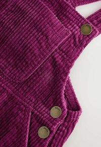Salopette in corduroy viola con texture rigata verticale, tasche quadrate e due bottoni rotondi in ottone con incisione "NEXT".