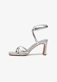 Silver high-heeled sandals with a square toe, thin ankle strap, and vamp straps. Smooth metallic finish with a 3-inch block heel.