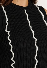 Mustriga musta kudumisest top, millel on ribikujundus ja mille esiosas on kaks valget volangiga triipu kontrastiks.