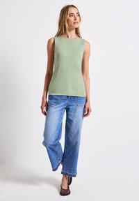 Ljusgrön ärmlös topp med rund halsringning, ihop med blekblå vida jeans och svarta nät skor. Enkel, avslappnad design.