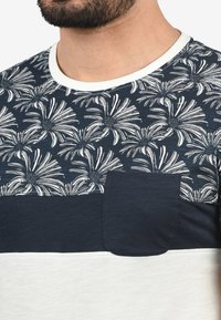 Kortermet t-skjorte med et marineblått blomstermønster, kontrasterende ensfargede marineblå og hvite paneler, og en brystlomme. Blandingsmateriale i bomull.