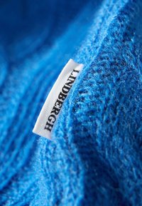 Strukturiert blauer Stoff mit einem sichtbaren Etikett, auf dem "LINDENBERG" steht. Der Stoff wirkt weich, fusselig und gestrickt.