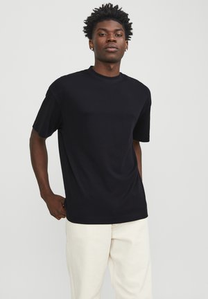 T-shirt noir à manches courtes en tissu doux, avec un col rond et une coupe décontractée, associé à un pantalon de couleur claire.