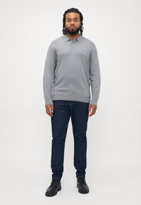 Grå langermet polo-skjorte med krage, paret med mørkeblå jeans og svarte støvler. Merkbar logo på skjorten. Glatt stofftekstur.