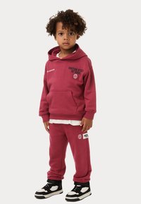 Bordeaux hoodie en sweatpants set, katoenmateriaal, voorzak, ribgebreide manchetten, met grafische tekstaccenten, gecombineerd met zwart-witte sneakers.