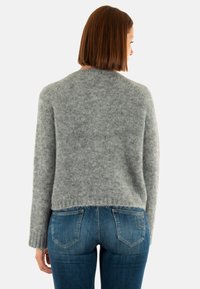 Suéter gris texturizado con cuello redondo, mangas largas y un dobladillo corto. Combinado con jeans de mezclilla azul que tienen bolsillos traseros.