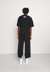 Svart kortärmad t-shirt med korta ärmar och en etikett bak, parat med vida svarta byxor, kompletterat med vita ankelstövlar.