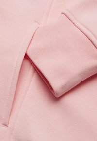 Tela de sudadera rosa claro con una superficie texturada y puño doblado, con un bolsillo lateral que tiene un detalle de costura limpio.