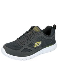 Zapatilla deportiva negra y gris con parte superior de malla, puntera redonda, diseño con cordones y suela blanca acolchada. Presenta el logo de la marca en amarillo.