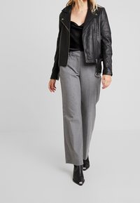 Černá kožená motocyklová bunda přes černý saténový top, doplněná světle šedými širokými kalhotami a černými kotníkovými botami se stříbrnými detaily.