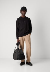 Μαύρη φουτερ με μικρό λογότυπο, μπεζ παντελόνια και μαύρη τσάντα γυμναστηρίου. Λείες υφασματικές υφές με πρακτικές λεπτομέρειες και απλό καπέλο.