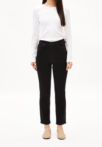 Jean noir taille haute assorti à un haut blanc à manches longues et col rond. Tissu doux avec une texture lisse. Chaussures beige à enfiler.