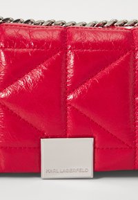 Borsa a tracolla in pelle trapuntata rossa brillante con motivo triangolare e placca logo argento. Dettaglio della tracolla in catena argentata.
