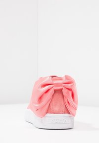 Sneaker in suede rosa con un grande fiocco in satin sul retro e una suola in gomma bianca. Superficie testurizzata e dettaglio del logo sul tallone.