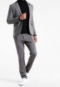 Grå ullblazer med en svart polo, tillsammans med grå byxor och vita sneakers. Klädseln har en knapp och skräddarsydd passform.