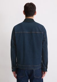 Donkerdenim jasje met een gestructureerd ontwerp, met een kraag en zichtbaar stikken, vanuit de achterkant weergegeven. Lange mouwen en zijzakken.