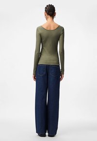 Olivenfarbene Langarmbluse mit Rundhalsausschnitt, kombiniert mit locker sitzenden dunkelblauen Jeans mit Gesäßtaschen und geradem Schnitt.