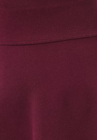 Burgundin neulekangas, jossa on sileä pinta; siinä on leveä vyötärönauha ja hieman k tapered muotoilu tyylikkään ilmeen saavuttamiseksi.