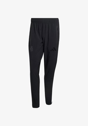 Čierne športové nohavice s elastickým pásom, vreckami na zips, logom Adidas na pravej stehne a erbom Realu Madrid na ľavej stehne.