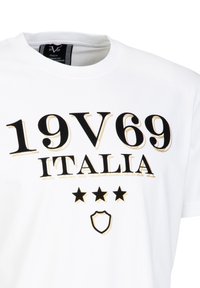Witte katoenen t-shirt met zwarte en gouden bedrukte tekst "19V69 ITALIA" en drie zwarte sterren, met een schildgrafiek onderaan.