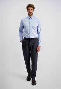 Lichtblauwe overhemd, donkergebloemde broek en zwarte schoenen. Het overhemd heeft een klassieke kraag; de broek heeft een trekkoord.