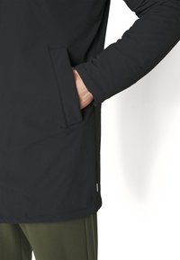 Black long coat with a smooth texture, featuring a side pocket and a straight cut. The sleeves are fitted, extending to the wrist.