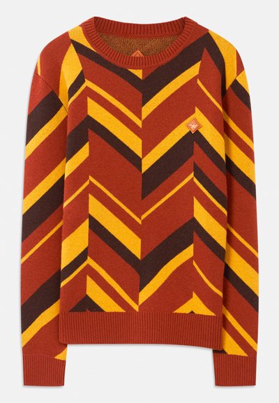 Långärmad stickad tröja med rostfärgade, gula och mörkbruna zigzag-ränder och en liten läderlogotyp på bröstet.