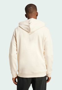 Cream hoodie with a drawstring hood, soft texture, ribbed cuffs and hem, and minimalistic design, worn by a person facing away.