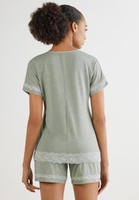 Ljusgrön bomullspyjamas med kortärmad topp och shorts, båda prydda med vit spetskant längs kanterna. Enkel och avslappnad passform.