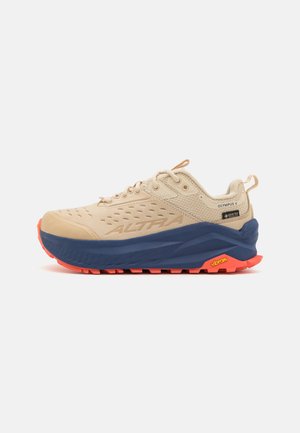 Beige terrengløpesko med strukturert overdel, blå mellomsåle og oransje yttersåle. Funksjoner inkluderer perforeringer og Vibram-logo.