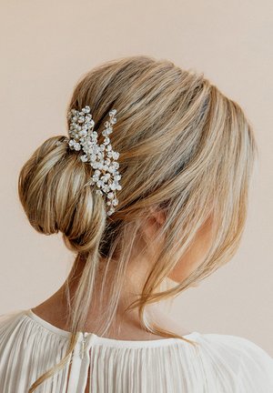 Accessorio per capelli con design floreale, caratterizzato da fiori bianchi su una delicata struttura in metallo dorato, indossato in un'acconciatura elegante a bun.