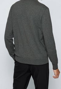 Szary sweter dziany o długich rękawach, z okrągłym dekoltem, ściągaczami przy rękawach i na dole, charakteryzujący się gładką fakturą i minimalistycznym wzornictwem.