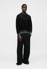 Μαύρο ριπ πλεκτό πουλόβερ με διαβάθμιση στο τελείωμα, με διακριτική πορτοκαλί λεπτομέρεια λογότυπου. Συνδυασμένο με άνετο μαύρο παντελόνι και επίπεδα παπούτσια.