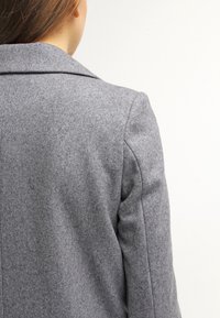 Blazer grigio in misto lana con bavero a punta, caratterizzato da cuciture sartoriali e una finitura testurizzata, mostrato da dietro.