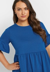 Blå bomullskjol med korta, utsvängda ärmar och samlad midja. Har en rundad halsringning och mjuk, texturerad tyg. Inga mönster eller detaljer.