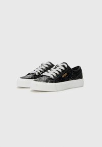 Svarta mönstrade sneakers med glänsande yta, med vita snören och gummisulor. Noterbar präglad logotypdetalj på sidorna.