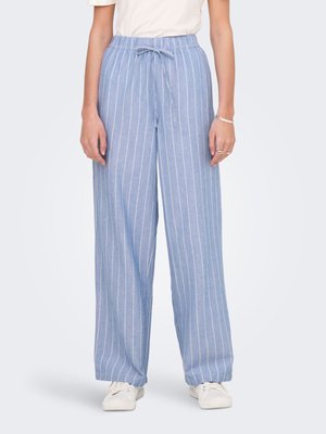 Pantalon bleu clair coupe décontractée avec des rayures verticales blanches, une taille élastique et un lien à l'avant, porté avec des chaussures blanches et un haut blanc.