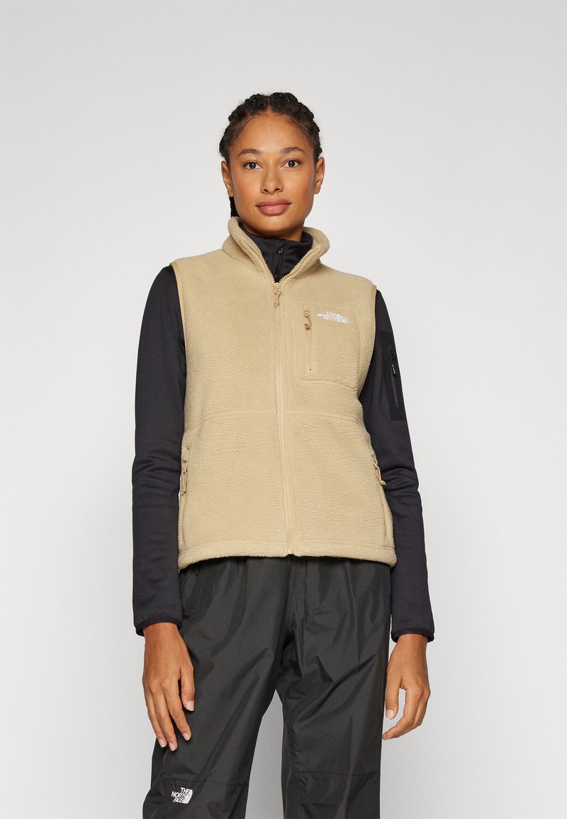 Beige fleece vest met hoge kraag, rits aan de voorkant en een borstzak. Draagt over een zwart T-shirt met lange mouwen, met een logodetail.