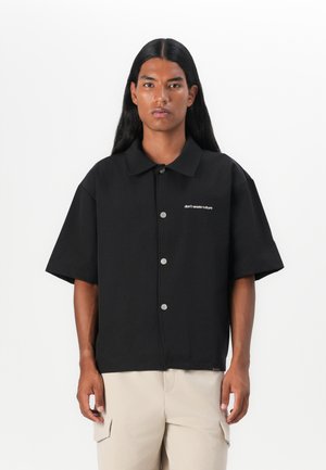 Black short-sleeve shirt with a pointed collar, silver buttons, and white "don't waste culture" embroidery on the left chest. Soft texture.