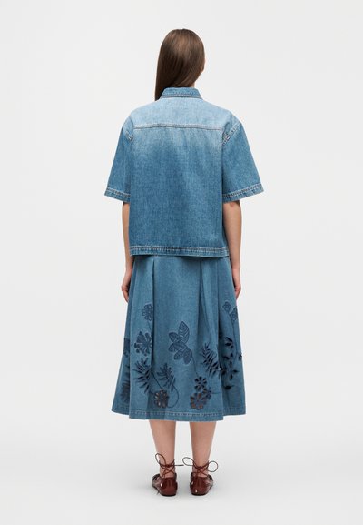 Τζιν μπουφάν με κοντά μανίκια, συνδυασμένο με φούστα μέχρι το γόνατο που έχει μπλε κεντητά λουλουδένια σχέδια σε πιο ανοιχτό τζιν ύφασμα.